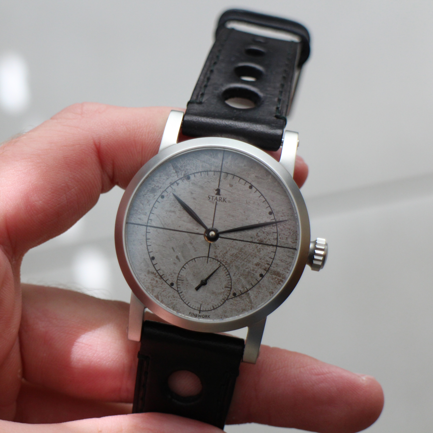 Hand holding a vintage-style watch with a black leather strap